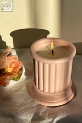 A lit blush pink pillar candle with vertical fluting for a wild roses luxury scented candle