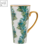 Tall white ceramic winter palm latte mug with gold rim and handle featuring vibrant teal and green tropical fern design