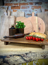 Rustic wooden pata board with dark brown finish holding cherry tomatoes loaf of bread and vintage metal containers