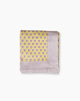 Folded cotton tablecloth with vibrant yellow background purple skull motifs and lavender textured edges