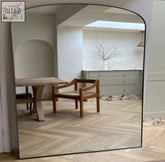 A sleek yoko 120x95cm black metal gentle arch mirror with minimalist frame reflecting warm wooden furniture