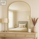 Yoko mirror with a gold steel frame and gentle arch design reflecting a bedroom interior 120x95cm size