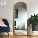 A tall yoko gold metal gentle arch mirror with a sleek gold frame stands against the wall measuring 150cm by 60cm