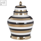 A sleek small ceramic jar with bold black white and gold horizontal stripes and a matching lid with golden finial