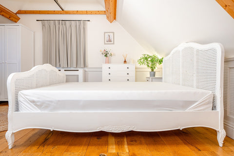 White cane bed frame with ornate carvings and woven rattan headboard paired with 100 percent organic bamboo flat bed sheets