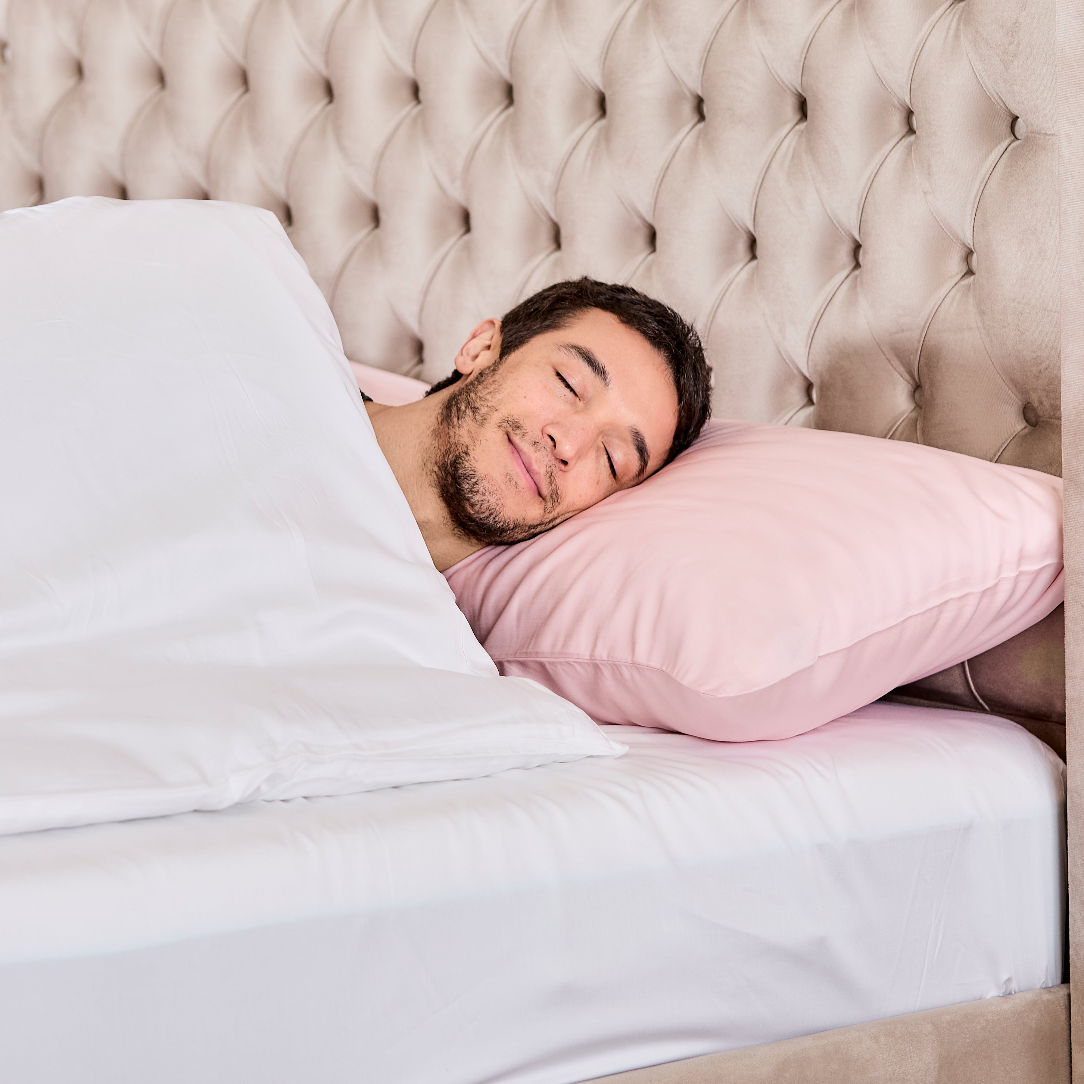 A man sleeps peacefully on a bed with soft pink 100% organic bamboo silk pillowcases nestled against a beige headboard