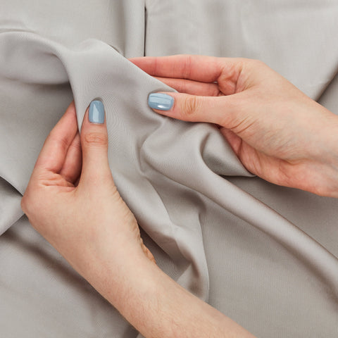 Light gray smooth textured 100% organic bamboo silk pillowcases gently held by hands with matching light blue nails