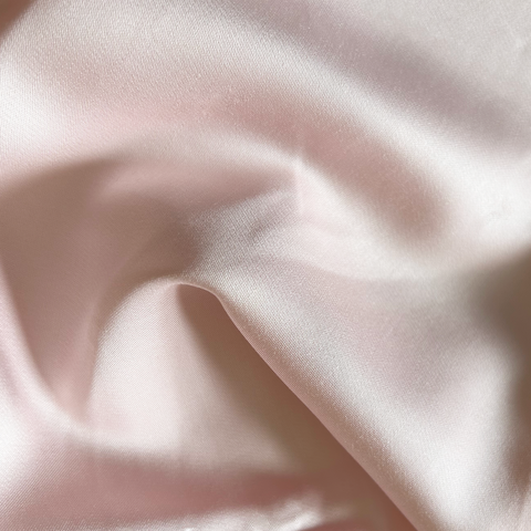 A soft blush pink 100% organic bamboo silk pillowcase with smooth glossy satin finish and gentle folds in a 2 pack