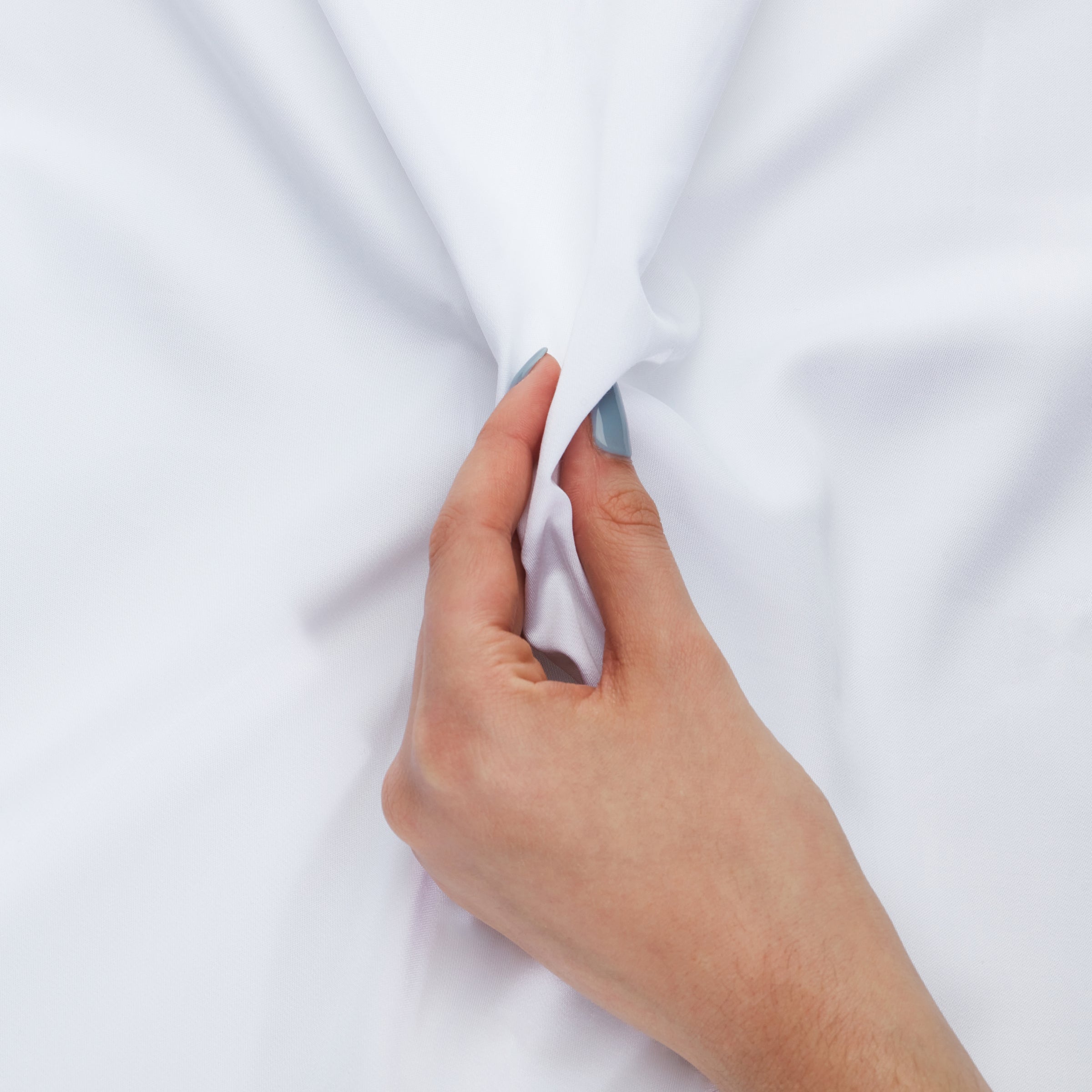A hand with light blue nails gently stretches a soft white 100% organic bamboo silk pillowcase two pack
