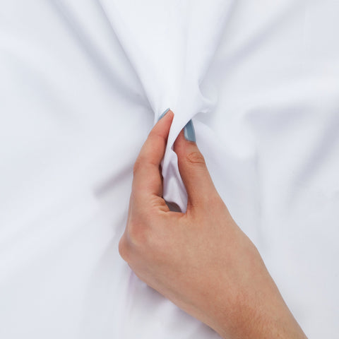 A hand with light blue nails gently stretches a soft white 100% organic bamboo silk pillowcase two pack