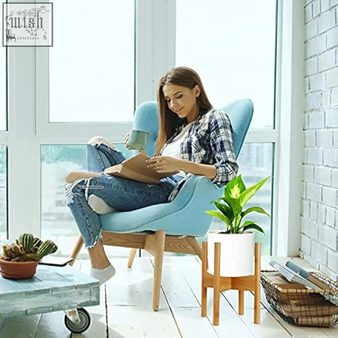 Light blue upholstered armchair with wooden legs next to a mid-century modern bamboo plant stand flower pot holder