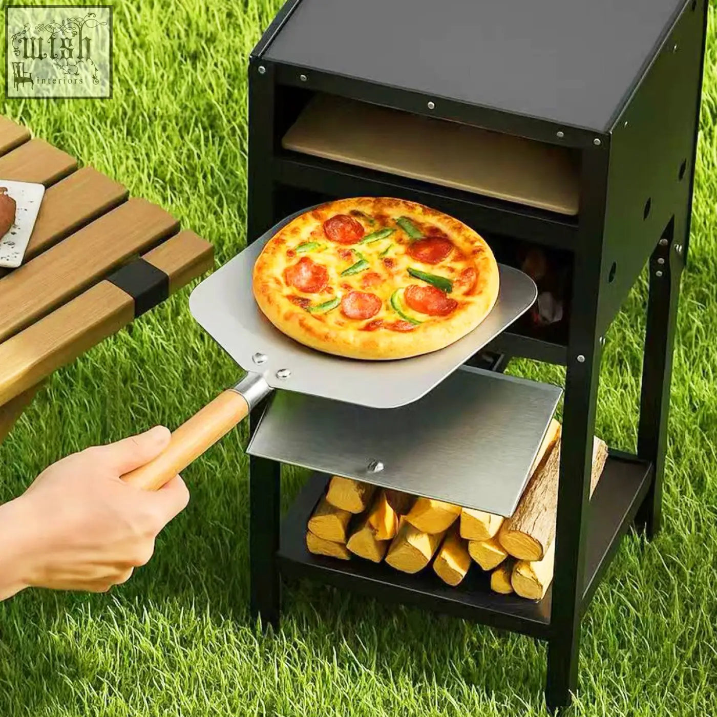 Freshly baked pepperoni and green bell pepper pizza on a metal pizza peel lifted from an outdoor pizza oven with black oxford cloth cover