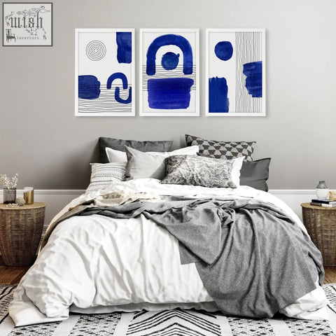 Three framed abstract wall art prints with bold blue brushstrokes and geometric patterns above a bed