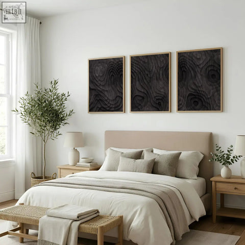 Beige upholstered bed with matching pillows and neutral throw blanket below abstract artwork dark charcoal topographic wave prints set of 3