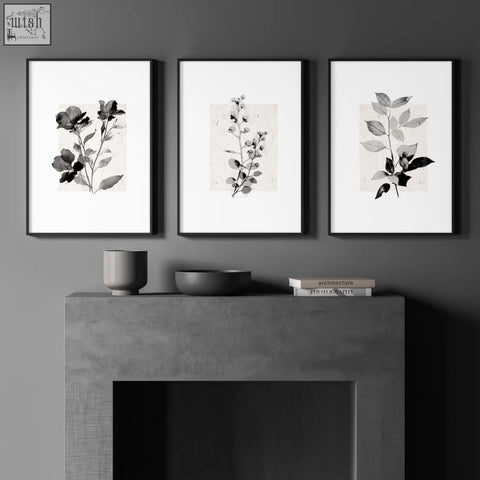 Three minimalist black-framed wall art prints featuring ivory and grey botanical studies on textured paper above concrete mantel