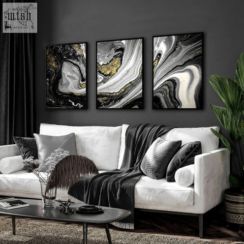 Three framed abstract wall art prints with black white and gold swirls hang above a modern living room sofa