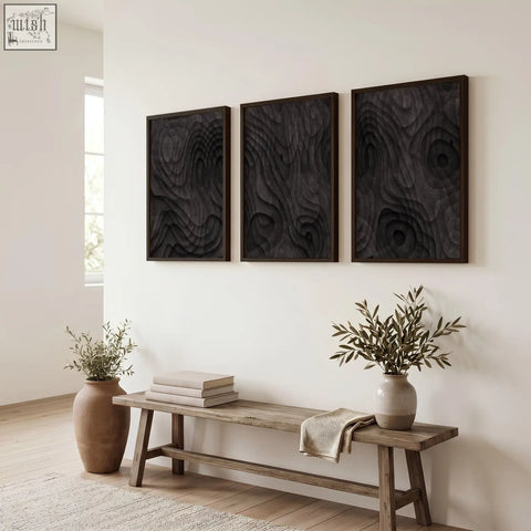 Three dark charcoal topographic wave abstract paintings with raised swirling texture in wood frames on white wall
