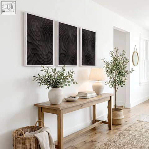 Light beige ceramic table lamp with soft linen shade next to abstract painting dark charcoal topographic wave prints set of 3
