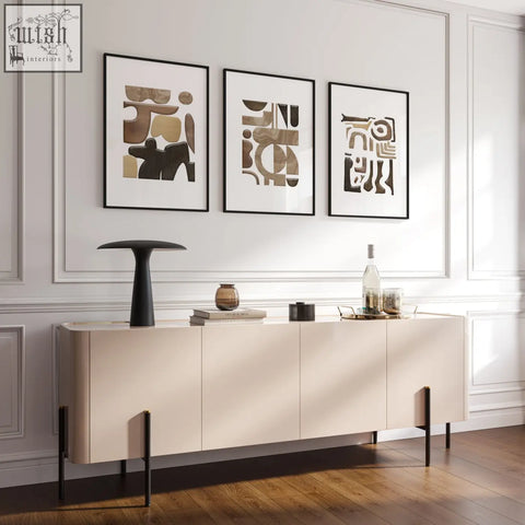 Cream-colored sideboard with sleek black legs shown below abstract wall art painting set of 3 prints on wall