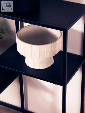 A white ceramic bowl with fluted design sits on a dark blue shelf of the acero black metal multi shelf unit