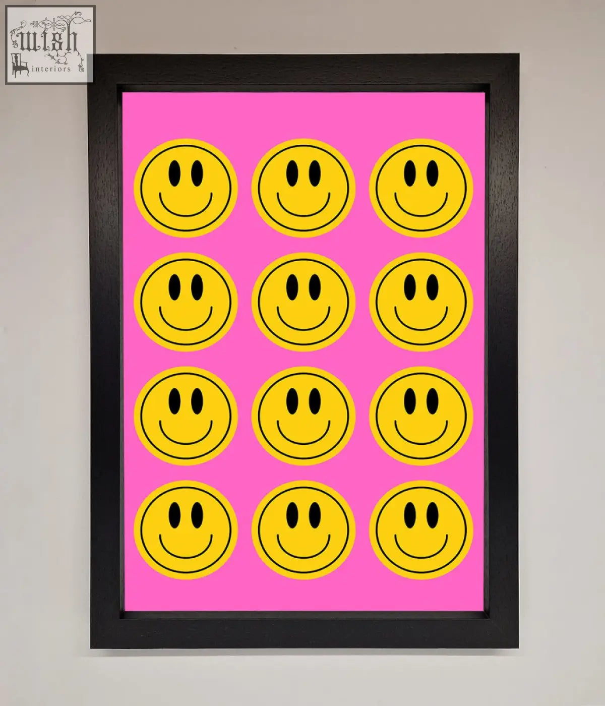A framed poster featuring bright yellow smiley faces on a vibrant pink background in a sleek black frame
