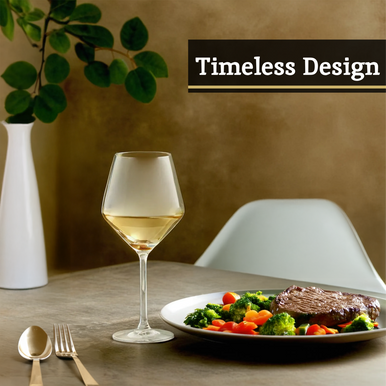 A clear crystal burgundy glass filled with white wine next to a plated steak and vegetables on a table