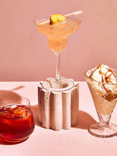 A clear martini glass with a pale orange cocktail garnished with citrus beside ada set of 4 crystal large tumblers