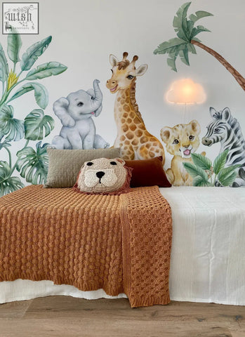 A cozy orange knitted blanket on a bed next to adorable safari wall decals with african animals stickers for kids room