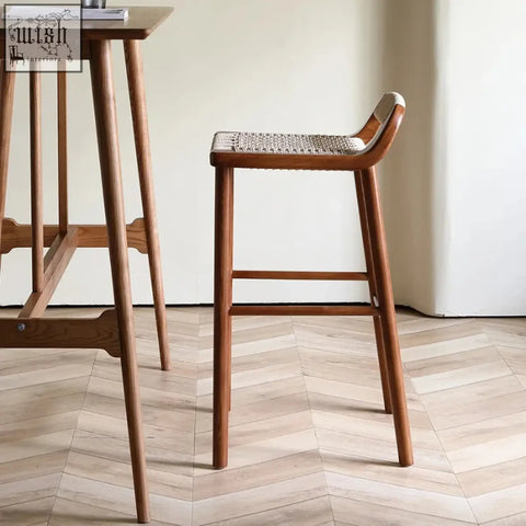 Aiko bar stool made of solid ash wood with a warm walnut finish and a woven cane seat with a curved backrest