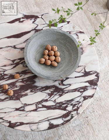 Aiko coffee table round marble with a gray stone bowl filled with walnuts on a white and burgundy marble tray stone coffee table