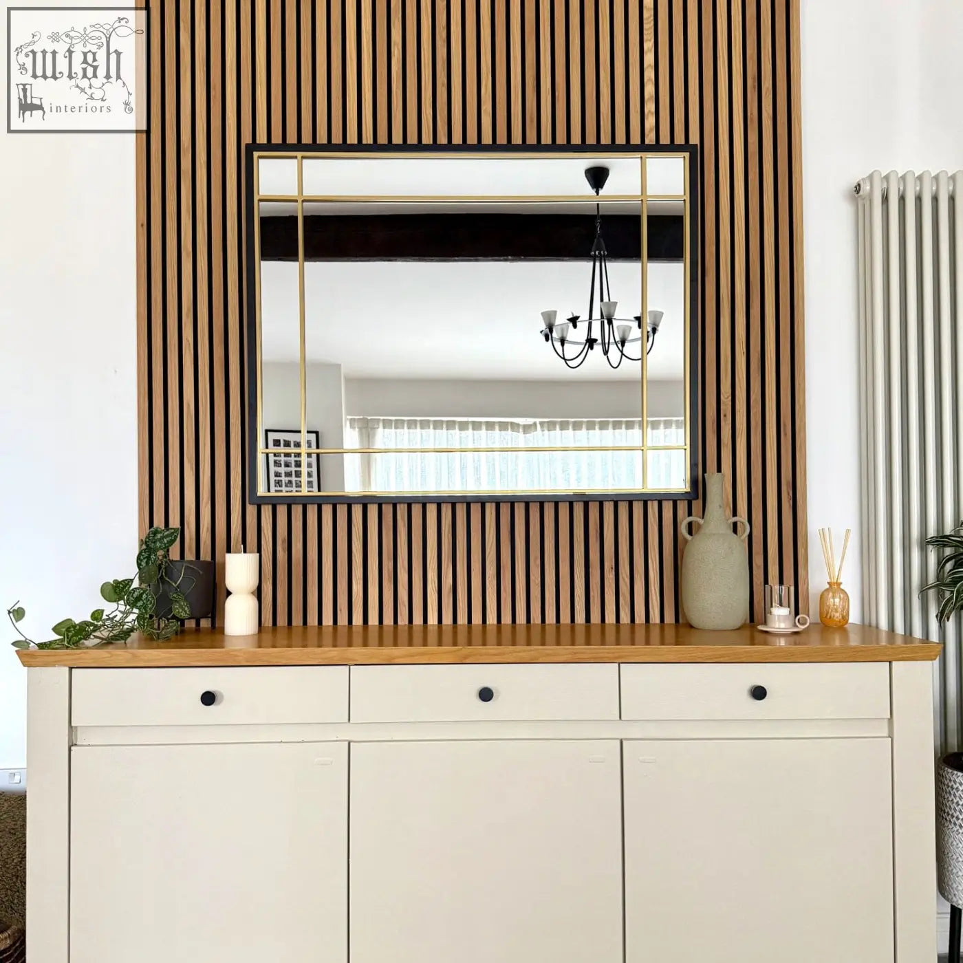Aimi black and gold metal frame window mirror mounted on wooden slat wall above white cabinet