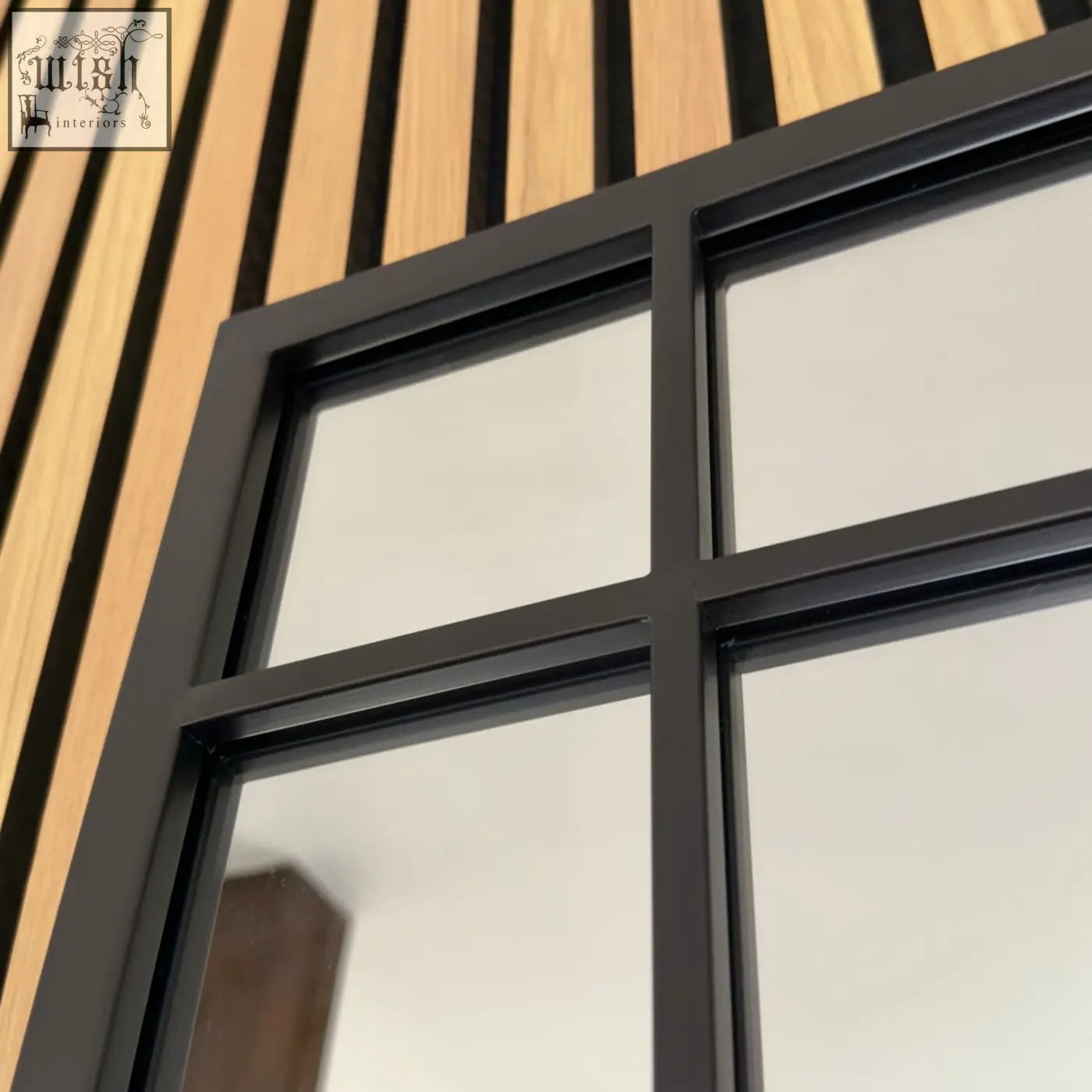Aimi black metal window mirror with four panes in a black metal frame set against a wood-paneled wall
