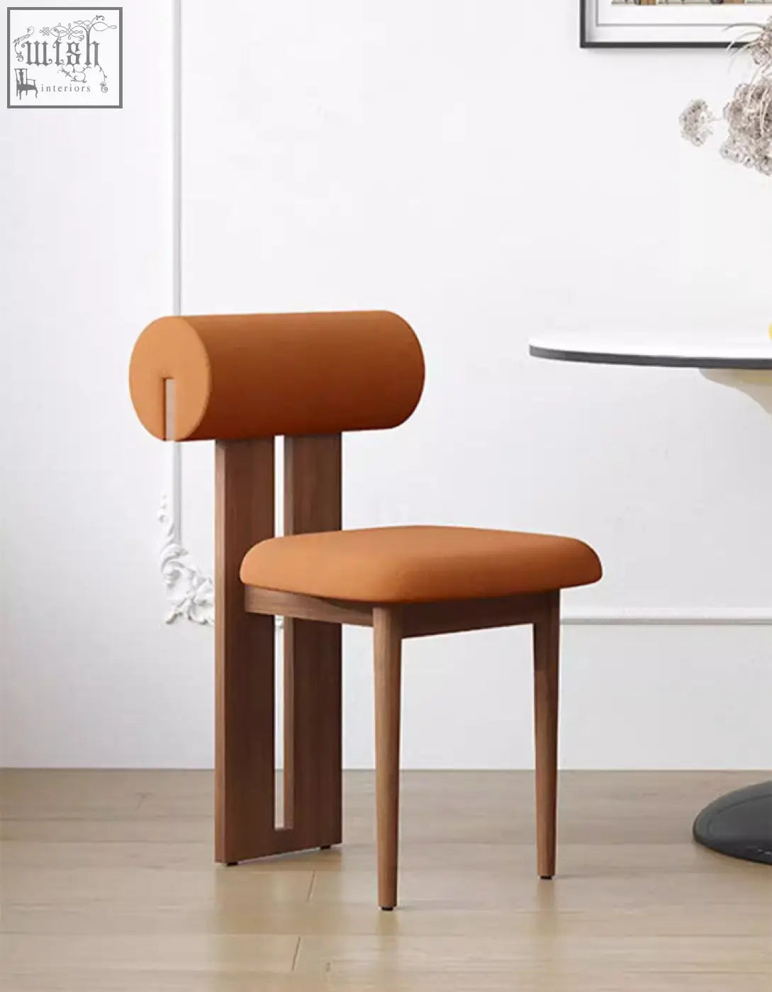 Airelle dining chair with warm orange upholstered cylindrical backrest and seat over dark wood legs in black brown