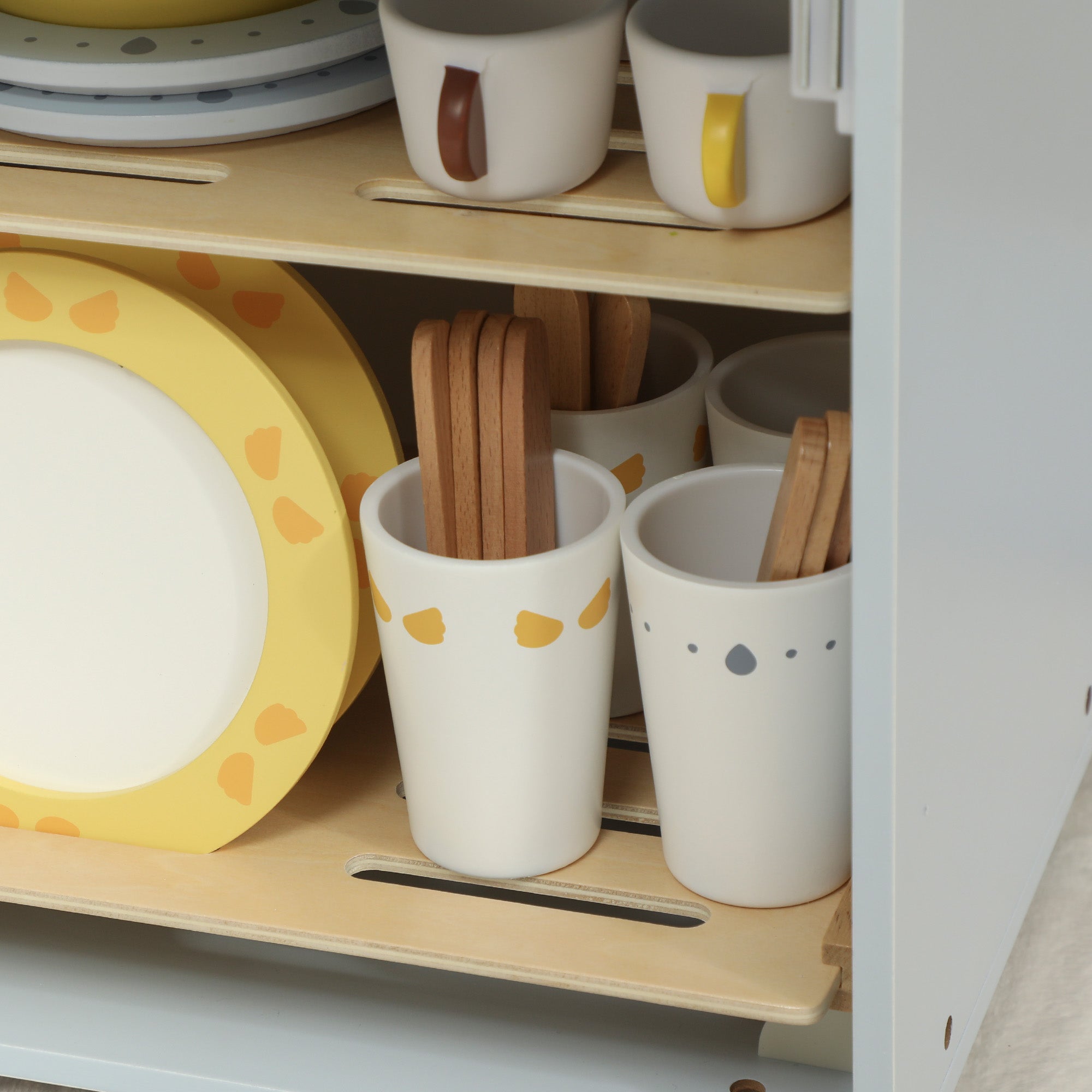 White ceramic utensil holders with yellow and gray dots holding wooden spoons from a wooden dishwasher playset