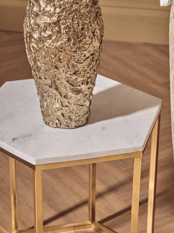 Akola gold textured small metal vase with a sculptural uneven surface sits on a hexagonal marble side table
