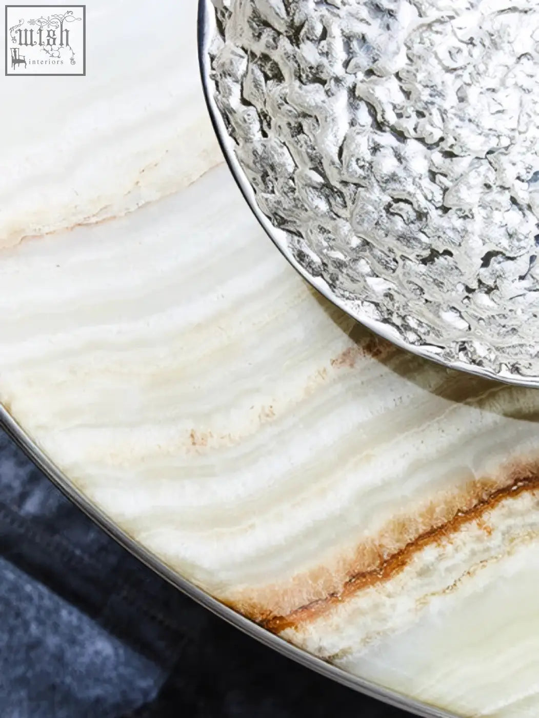 Silver textured decorative bowl with intricate leaf pattern resting on smooth layered white and beige stone surface