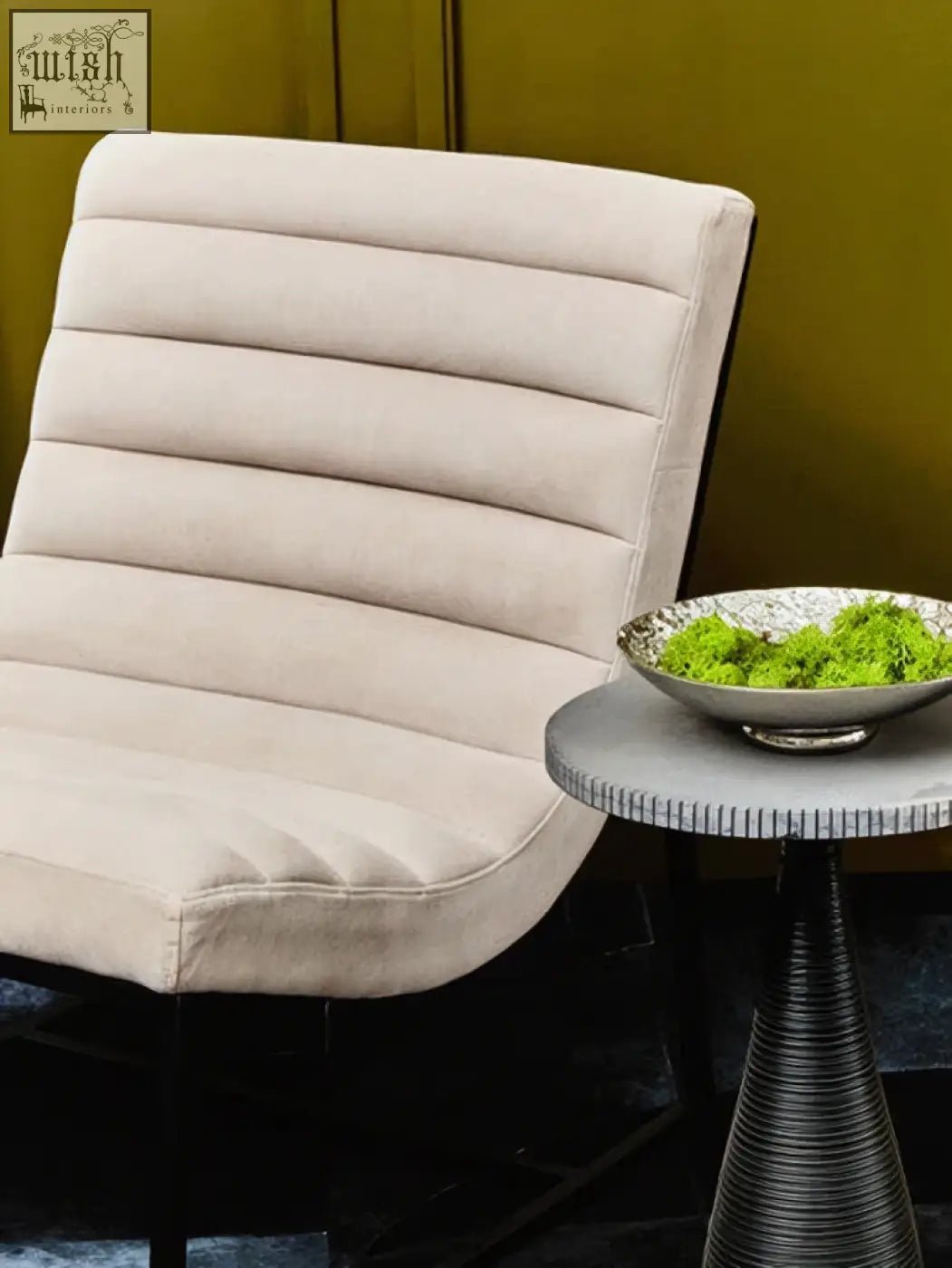 Beige upholstered armchair with vertical stitched panels and sleek black metal frame next to silver textured decorative bowl