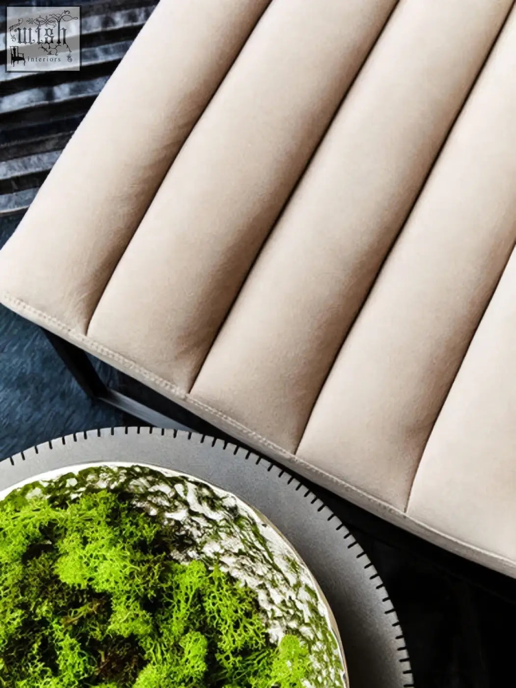 Beige upholstered bench with vertical channel tufting and black metal frame shown next to a silver textured decorative bowl