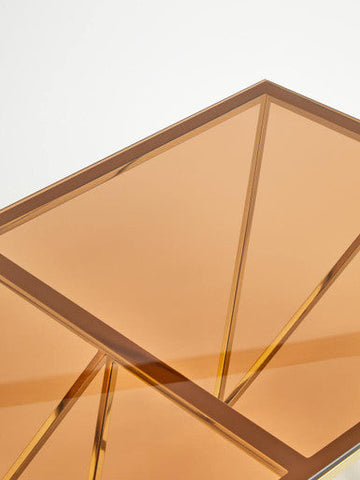 A geometrically framed amber acrylic tray on an allure champagne metal coffee table with prismatic legs