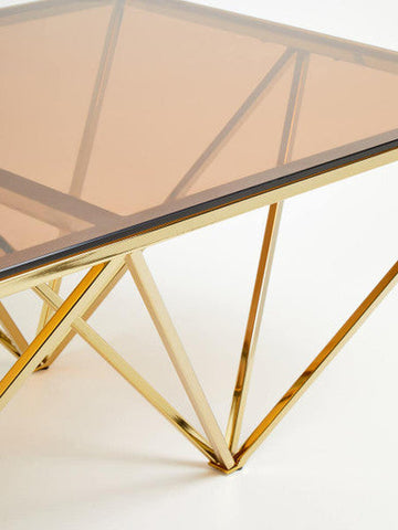Gold-toned allure champagne metal coffee table with prismatic legs and a translucent amber glass top