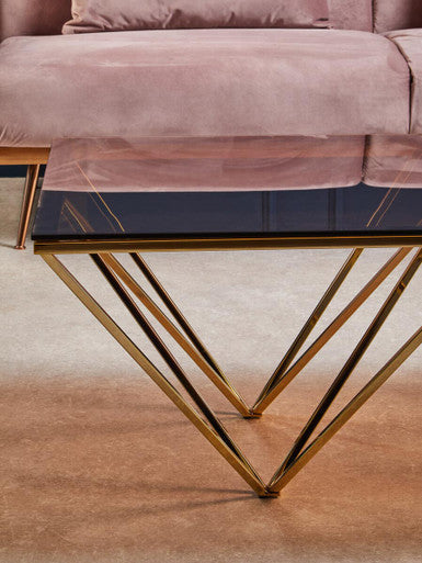 A sleek coffee table with a dark glass top and allure champagne metal prismatic legs in a modern geometric design