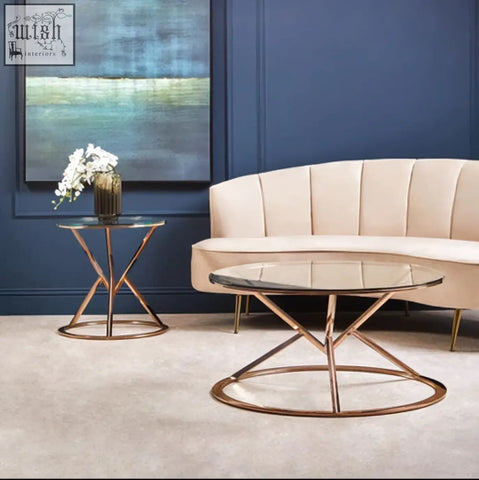 Modern rose gold coffee table with a corseted metal base and clear glass top perfect for stylish living spaces