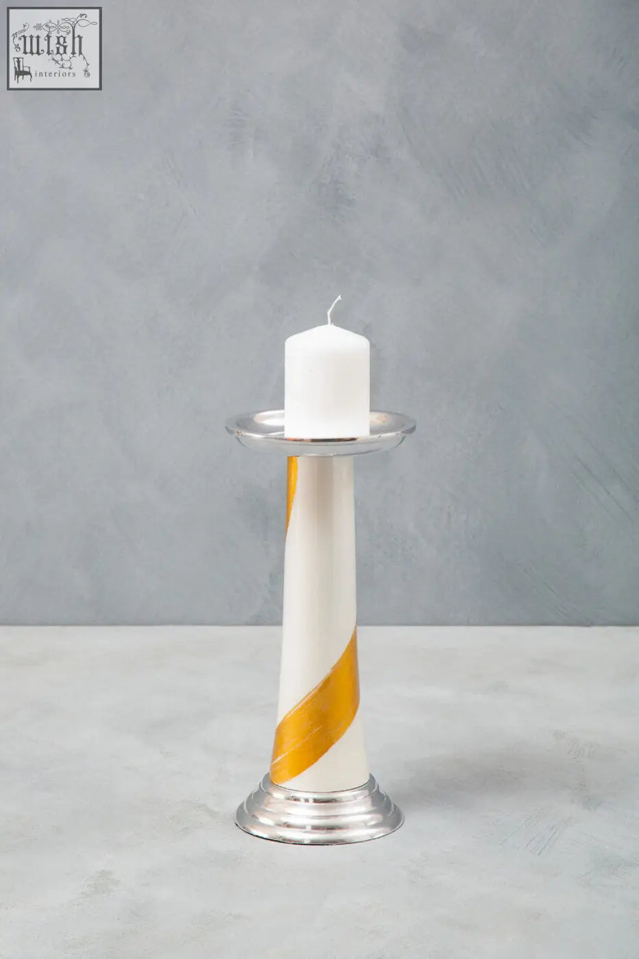 A sleek white candle with a gold stripe on a silver metal stand in the alma white and gold gold candle holder