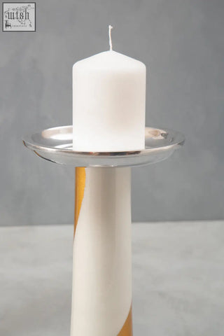 A sleek white candle on a polished silver dish with a tall gold candle holder featuring cream swirls