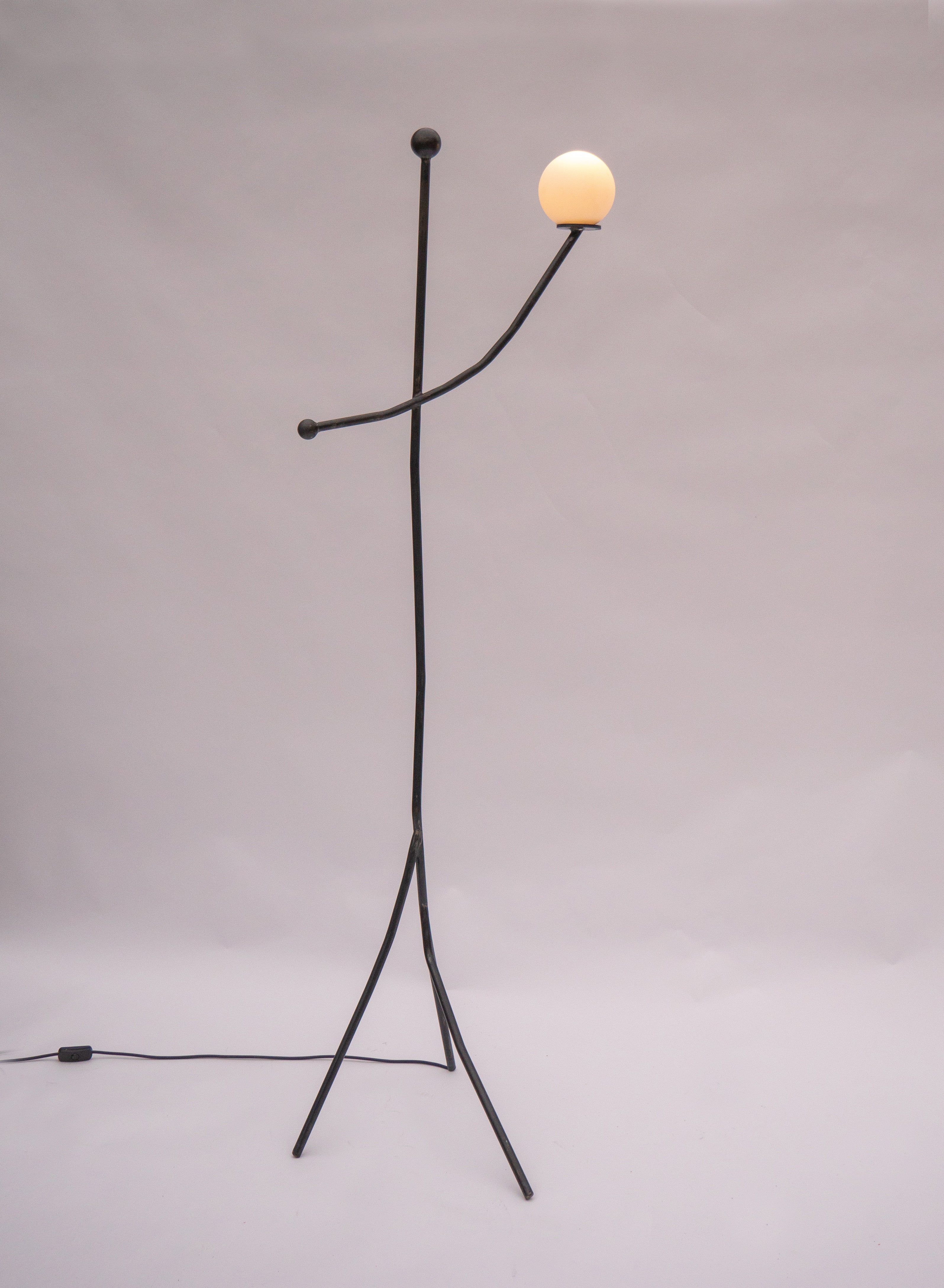Black metal aluminium balancing act floor lamp with minimalist stick figure design and warm spherical glass bulb