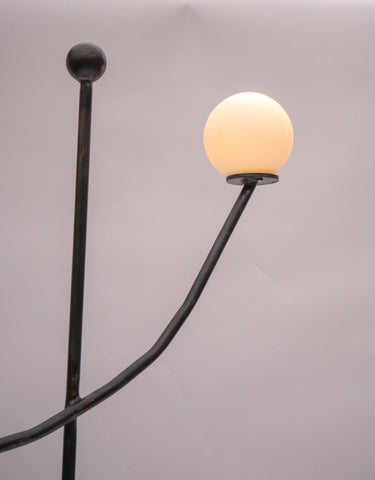 Black wrought iron aluminium balancing act floor lamp with curved arm and frosted glass globe shade illuminated