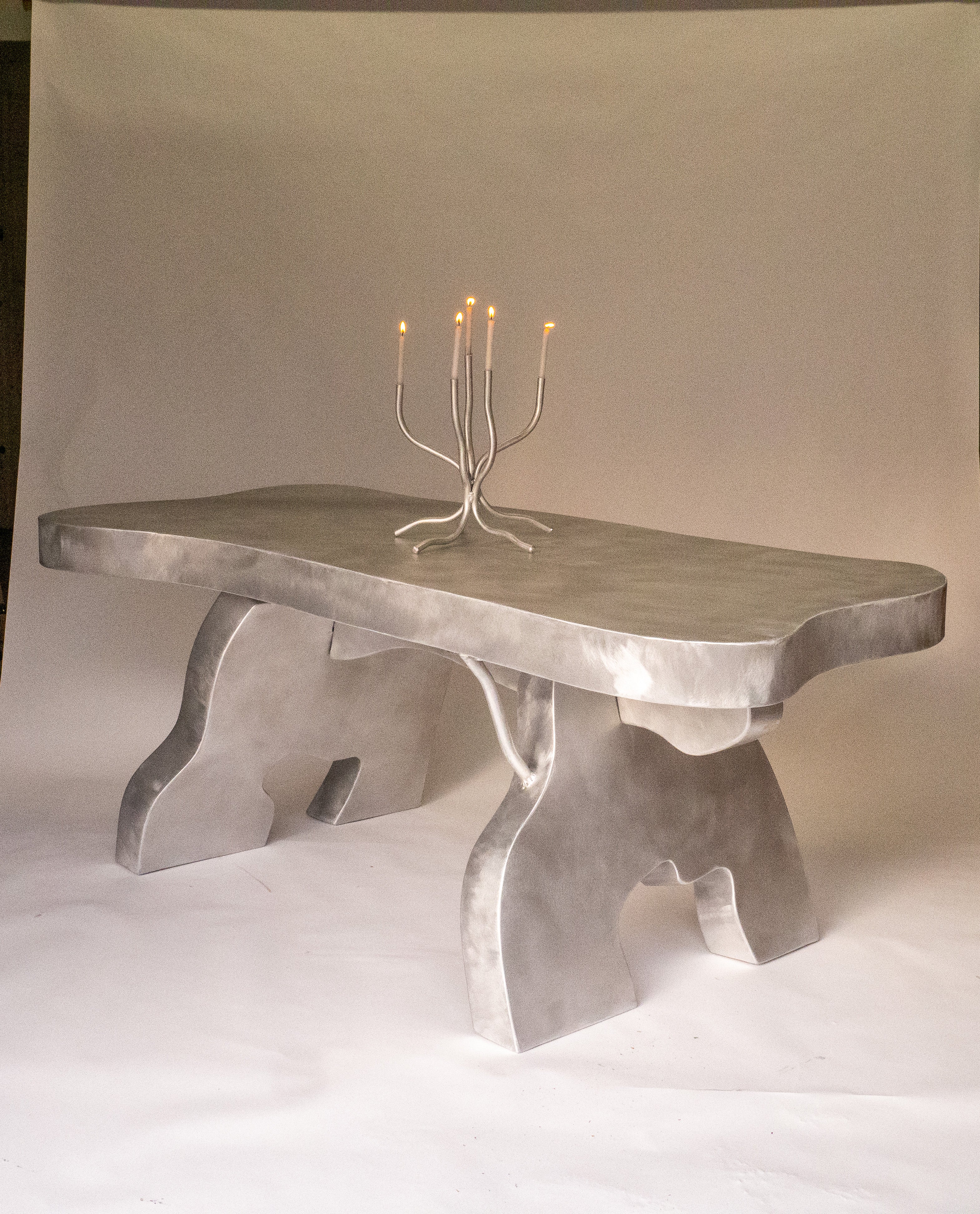 A silver metallic aluminium big table with sculpted organic legs and a smooth slightly uneven top surface
