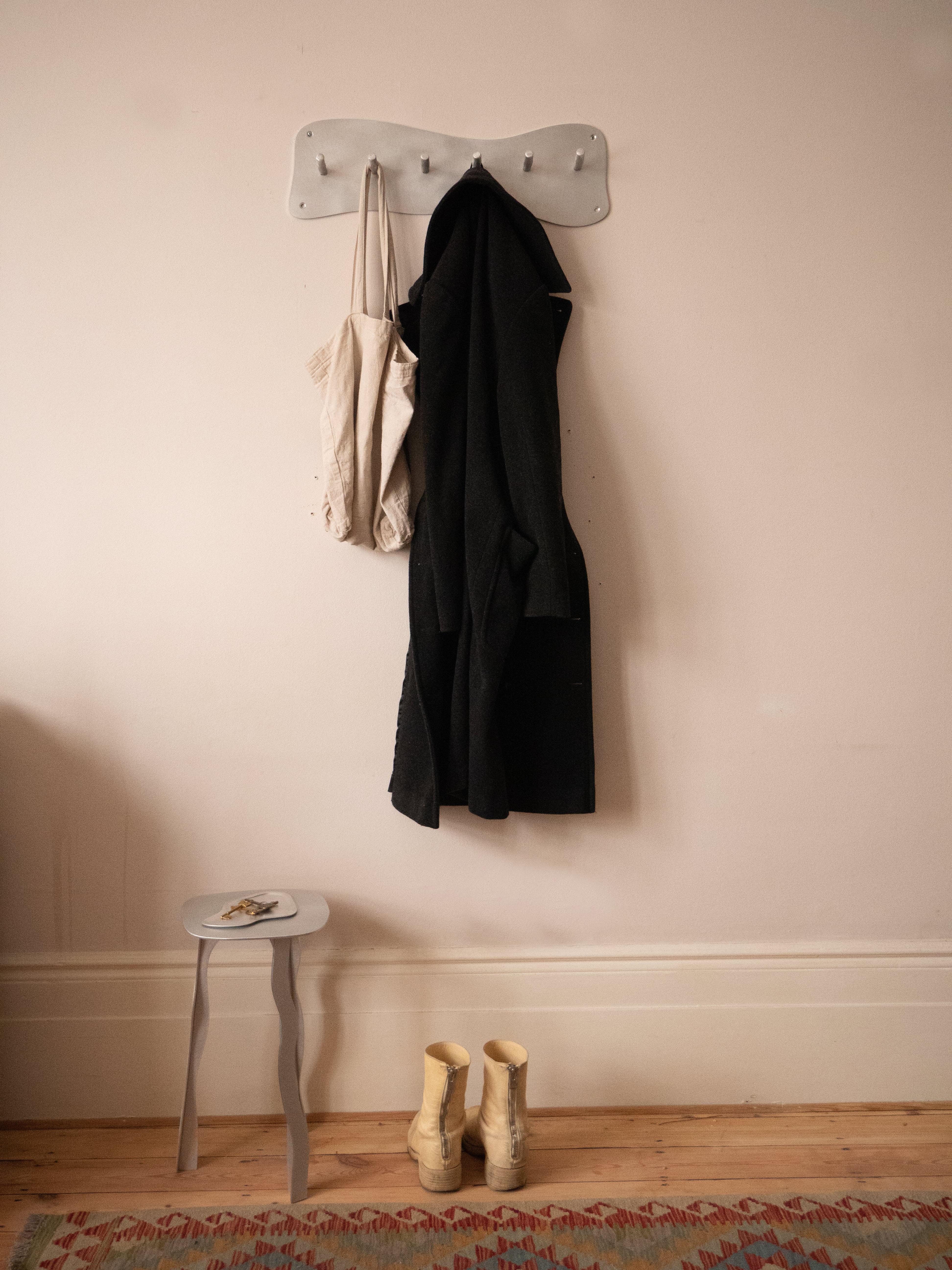 A minimalist white aluminium coat rack with five evenly spaced hooks mounted on the wall for hanging coats