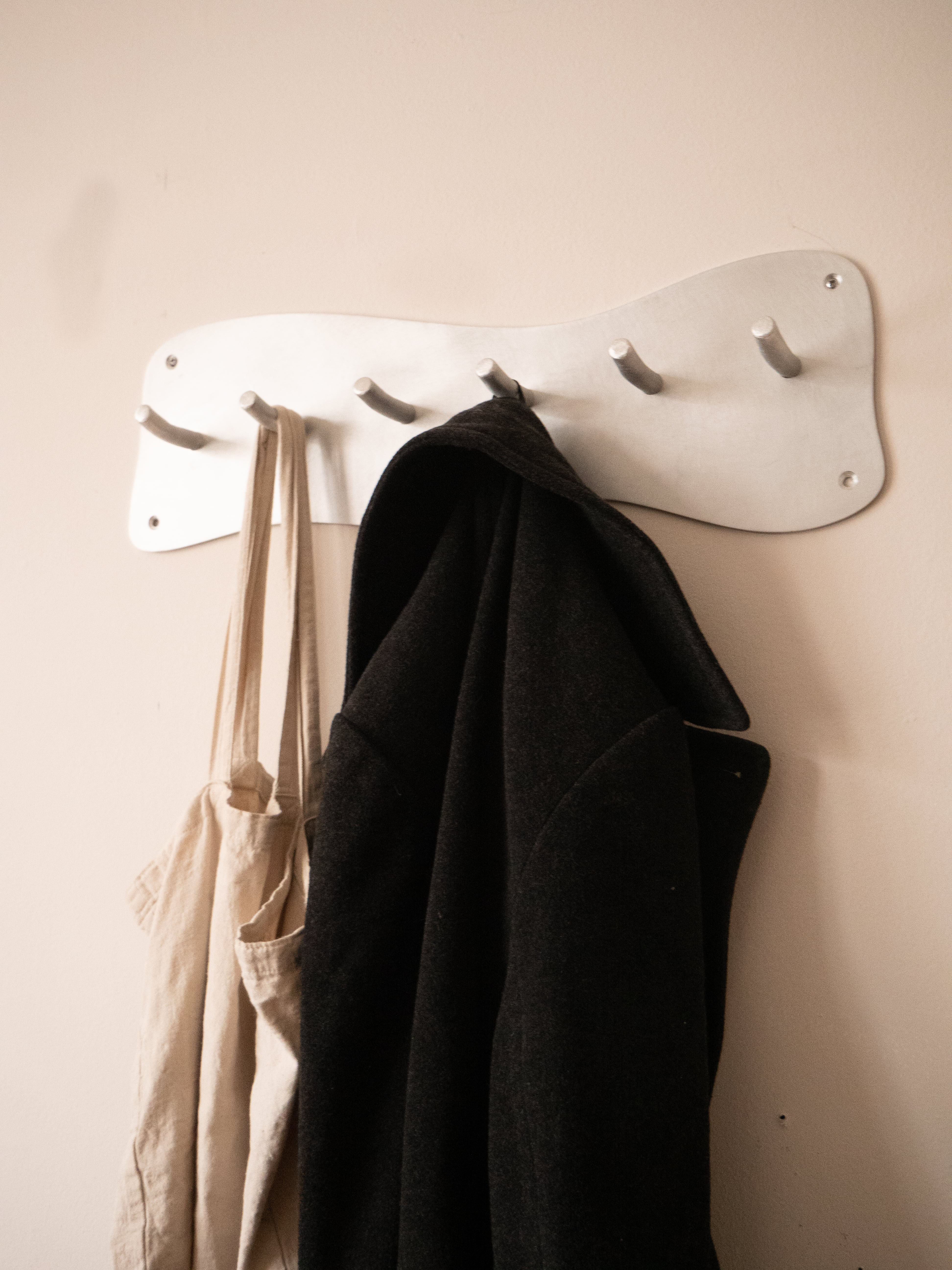 White aluminium wall-mounted coat rack with five curved hooks for hanging coats and bags