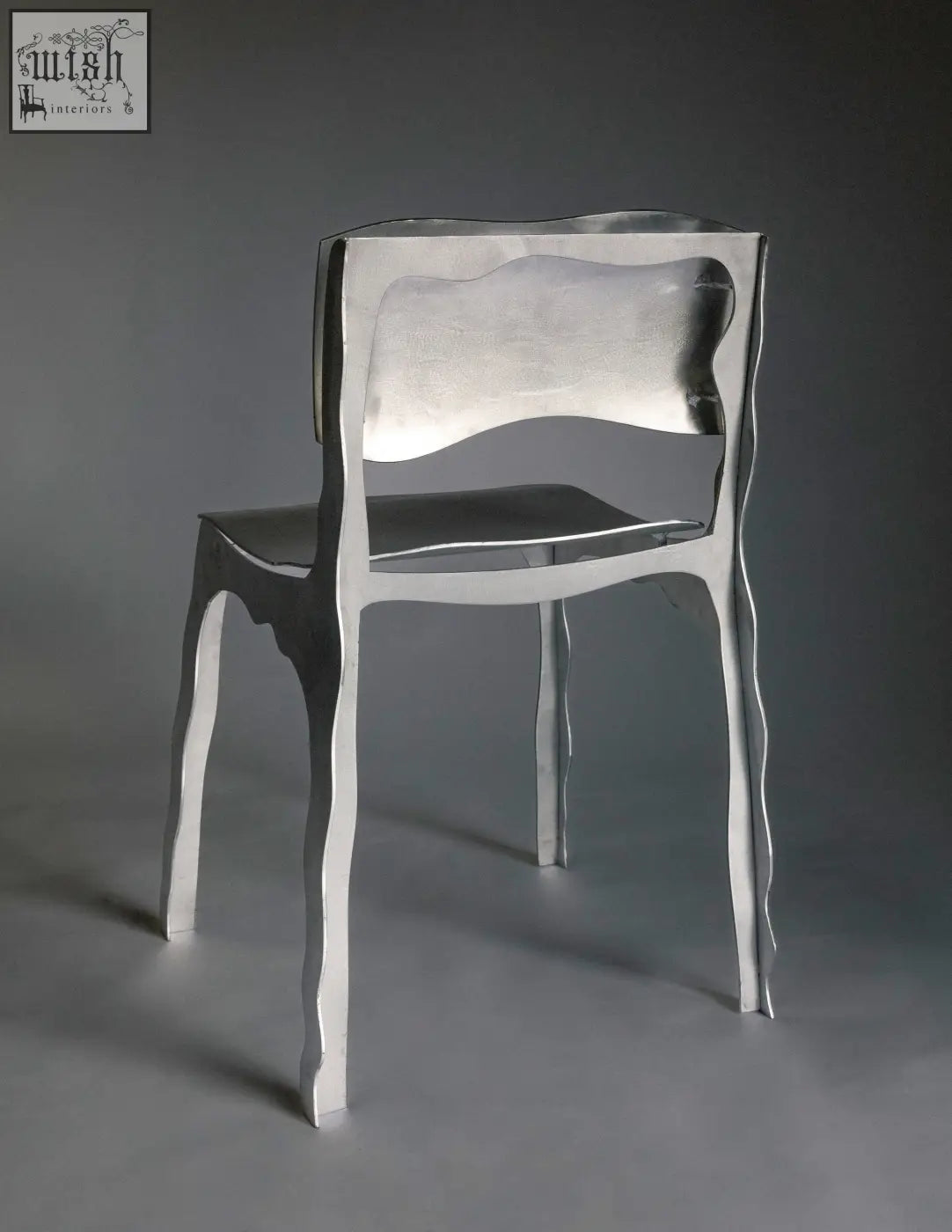 Silver metallic aluminium contemporary chair with sculpted flowing legs and reflective backrest shown from back side